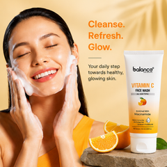 A woman with foaming face wash applied to her face is shown on a warm beige background beside a tube of balance Vitamin C Face Wash and sliced oranges.